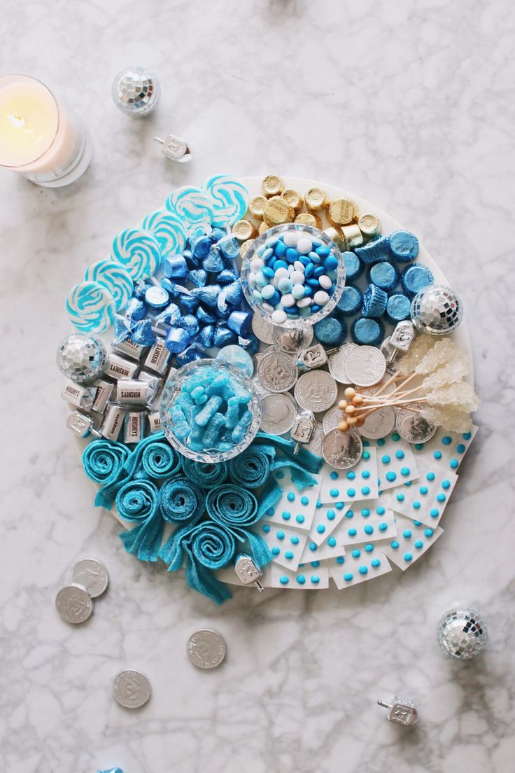 a plate with blue and white decorations on it next to a candle, some coins and candlesticks