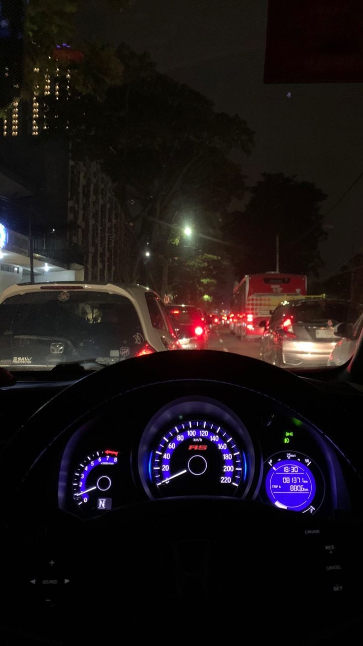 the dashboard of a car is lit up at night with many cars in the background