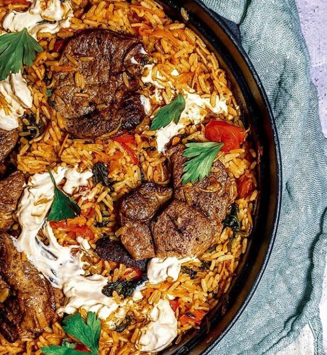 a skillet filled with meat and rice on top of a blue cloth next to a fork