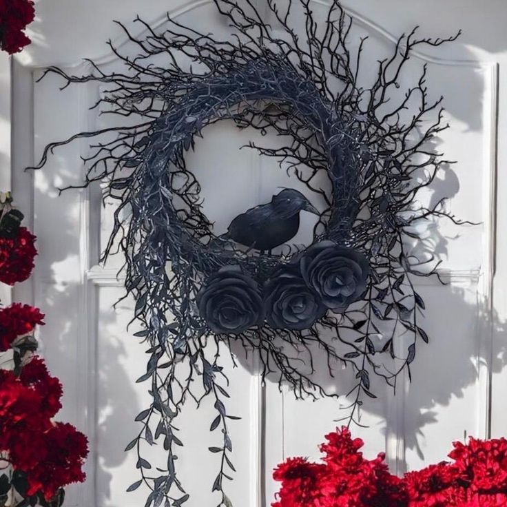 a black bird sitting on top of a wreath next to red flowers in front of a white door