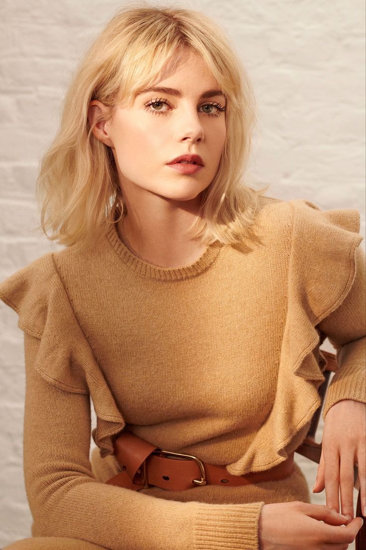 a woman with blonde hair wearing a tan sweater and brown pants sitting on a chair