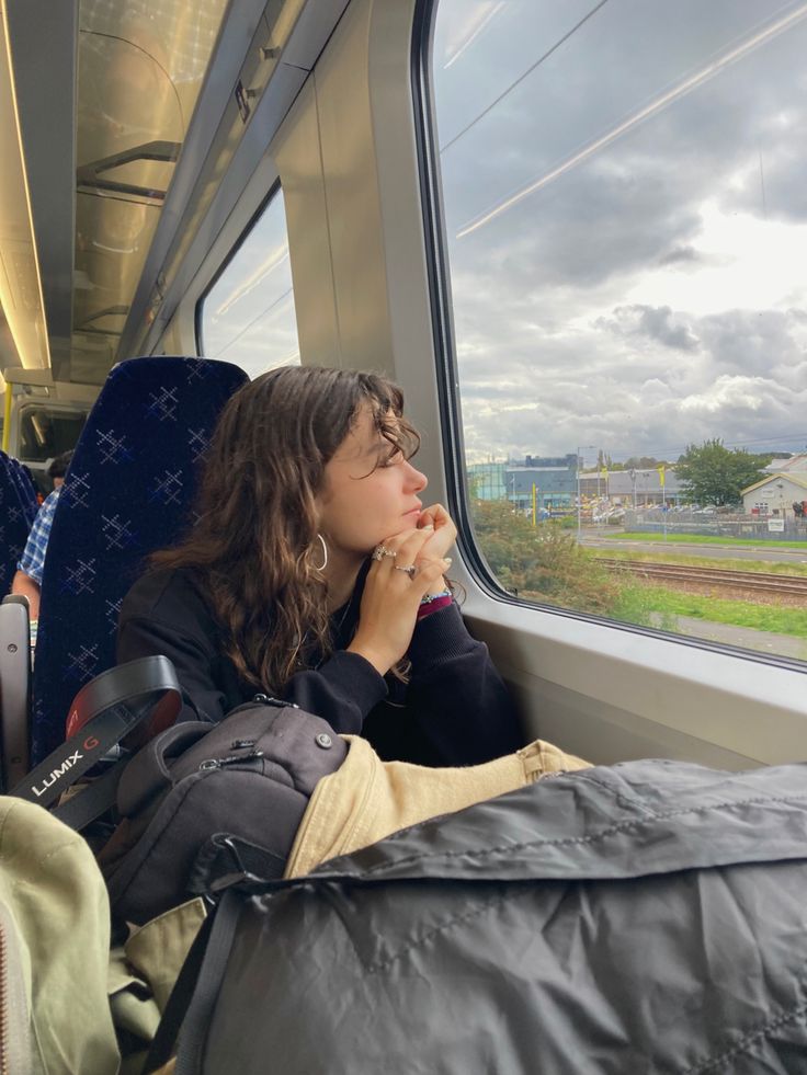 a woman sitting on a train looking out the window while holding her hand up to her mouth