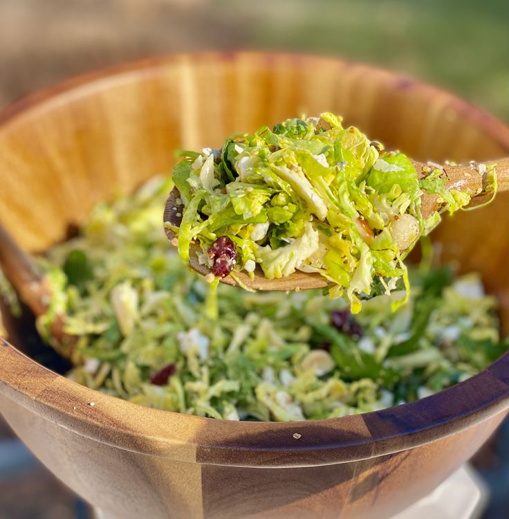 a wooden spoon full of lettuce and cranberry salad in a bowl