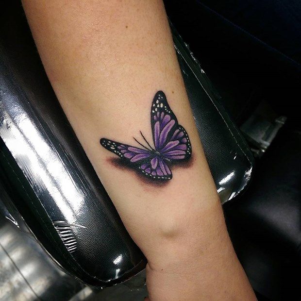 a small purple butterfly tattoo on the left forearm and right arm, sitting on a woman's leg