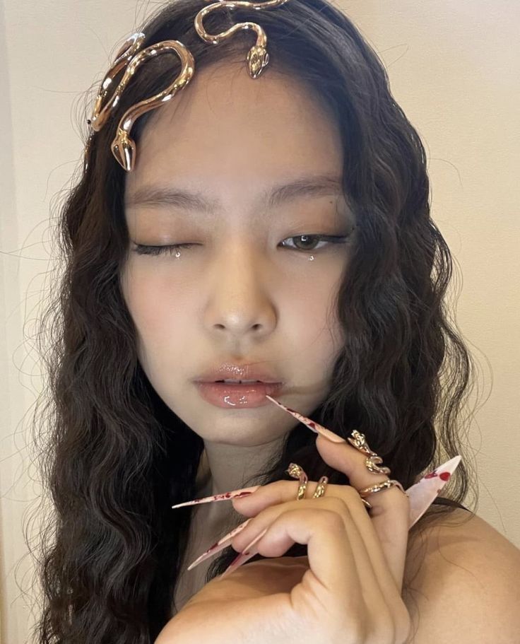 a woman with long dark hair and gold jewelry on her head is holding a pair of scissors in front of her face