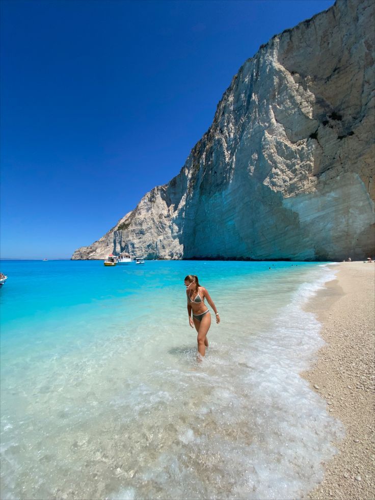 a woman is wading in the clear blue water at an empty beach next to a mountain