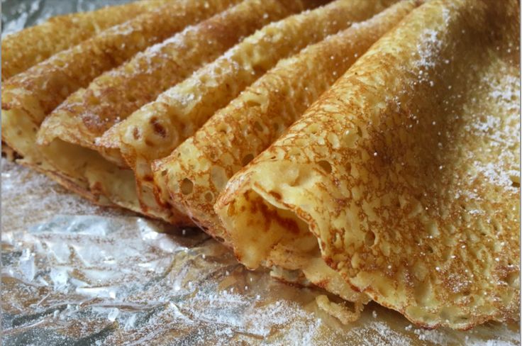 four crepes sitting on top of foil covered in powdered sugar