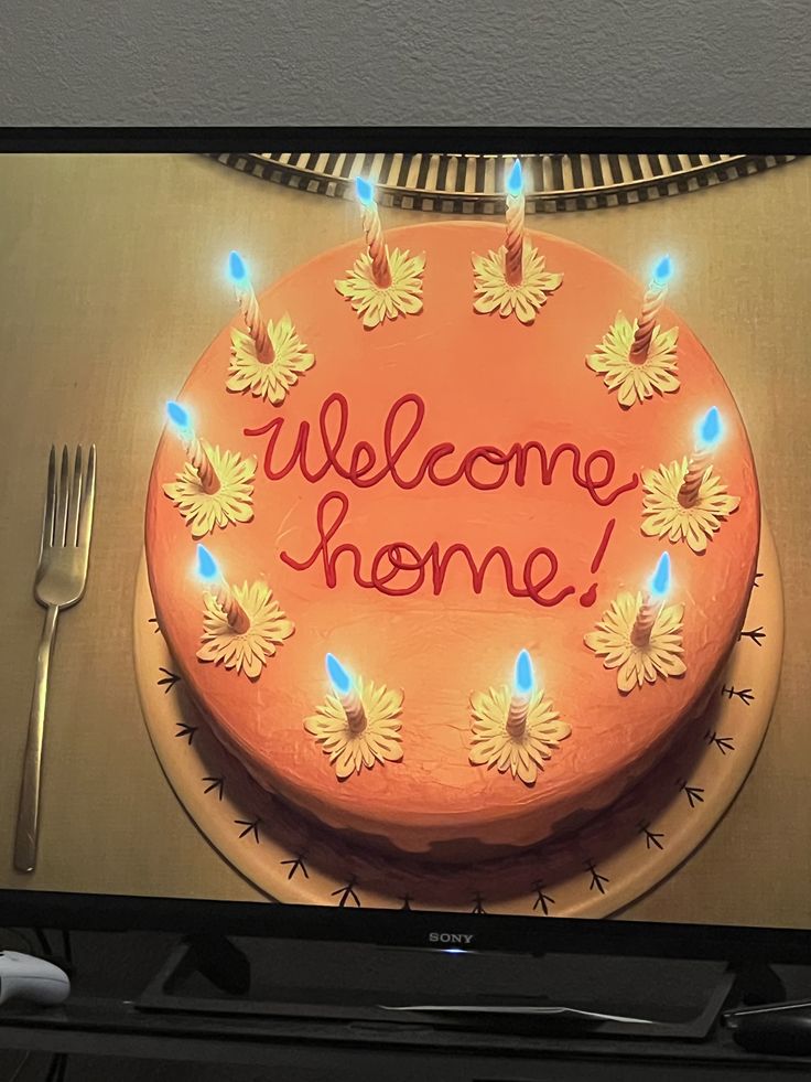 a welcome home cake on a flat screen tv with forks and knives next to it