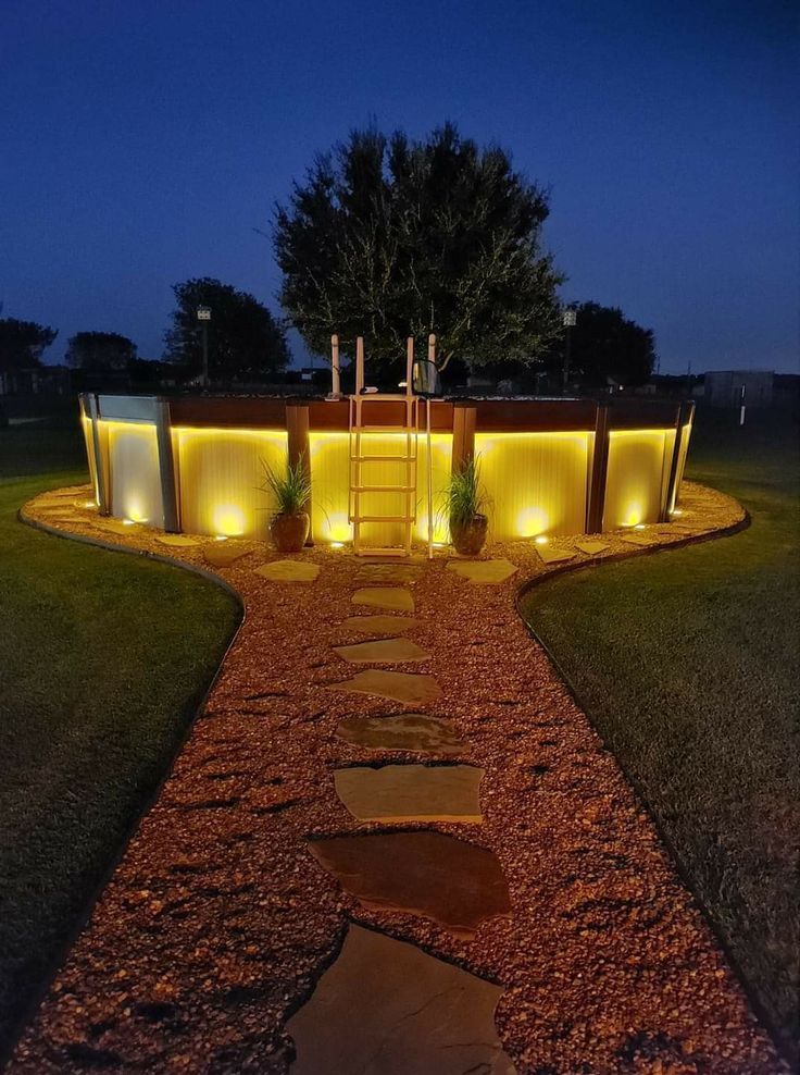 a pathway lit up with lights in front of a house at night, surrounded by grass and rocks