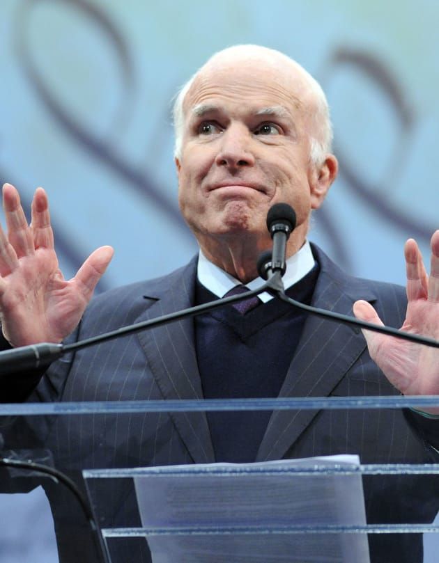 a man in a suit and tie standing at a podium with his hands raised up