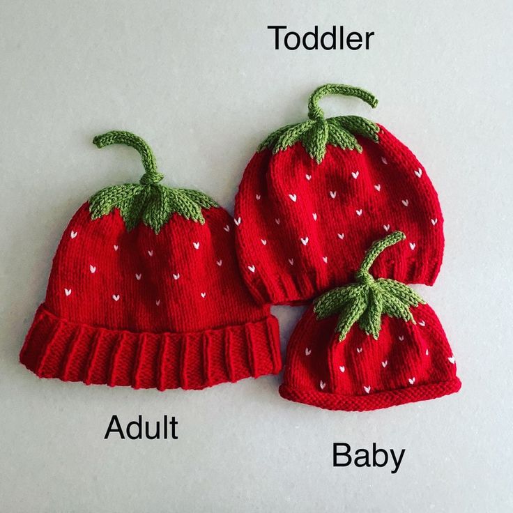 two red knitted strawberries sitting next to each other on top of a white surface