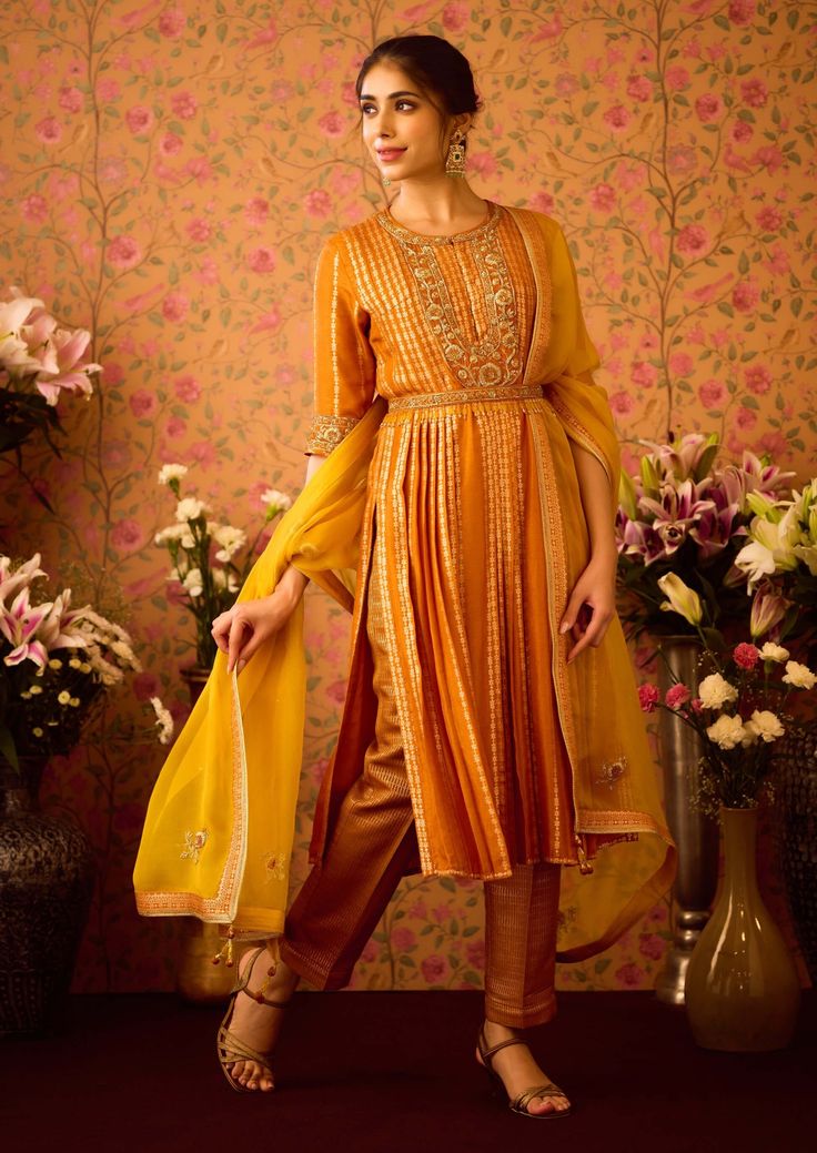 Step into refined elegance with the yellow mustard hand-embroidered pleated silk brocade kurta, perfectly paired with brocade pants. This exquisite ensemble features intricate hand embroidery that adds depth to the luxurious fabric, while the pleated design offers a graceful silhouette. An embroidered belt accentuates the waist, and the matching dupatta completes the look, making it an ideal choice for festive occasions and celebrations. Elegant Yellow Kurta For Navratri, Navratri Straight Kurta Sets With Gold Embroidery, Navratri Gold Embroidery Straight Kurta Set, Gold Silk Palazzo Set With Straight Kurta, Transitional Yellow Raw Silk Anarkali Set, Yellow Long Sleeve Raw Silk Kurta, Yellow Palazzo Set With Dabka Straight Kurta, Yellow Raw Silk Palazzo Set With Dabka Work, Gold Cotton Silk Palazzo Set With Dabka Work