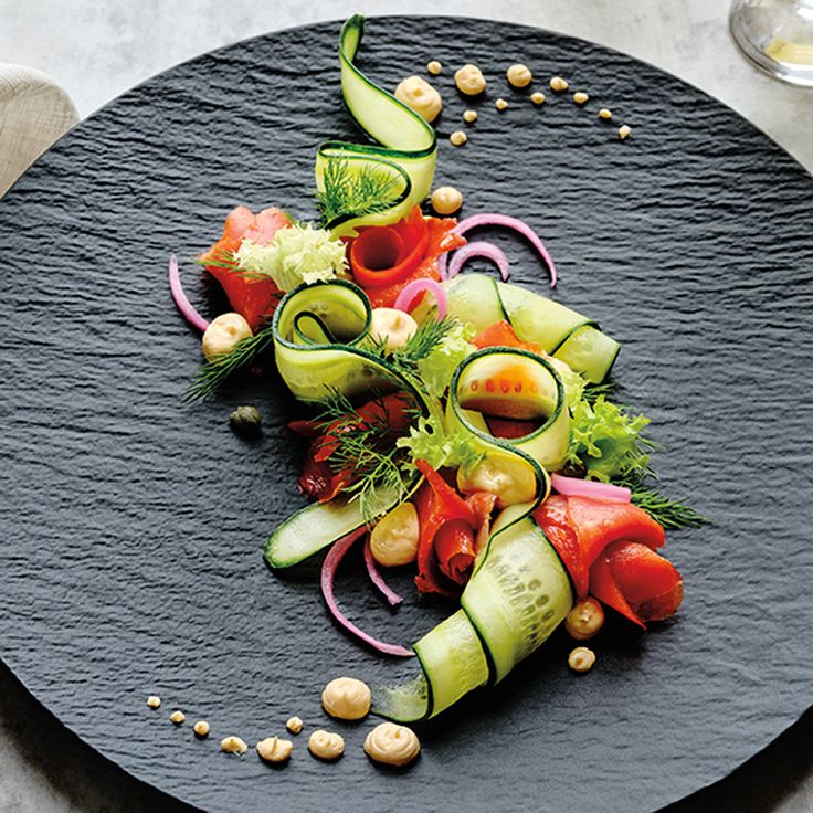 a black plate topped with cucumbers and other vegetables