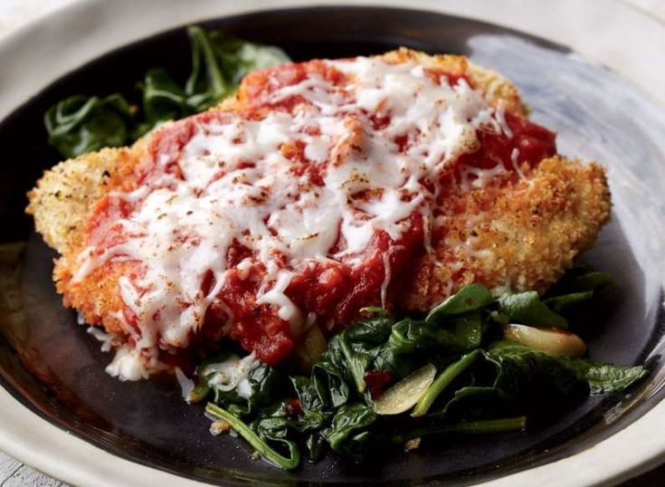 chicken parmesan with spinach leaves on a black and white plate, ready to be eaten