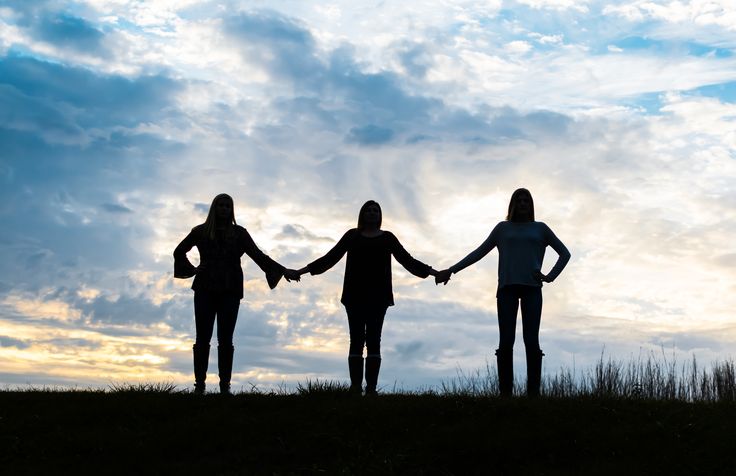 three people holding hands while standing on top of a grass covered hill under a cloudy sky