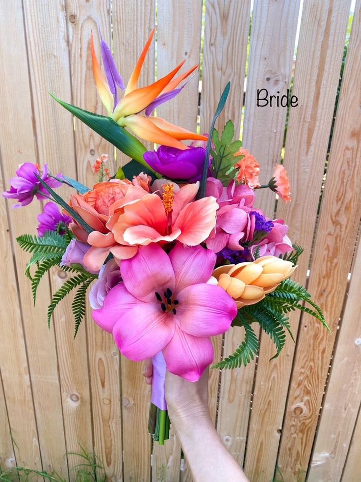 a hand holding a bouquet of flowers in front of a wooden fence