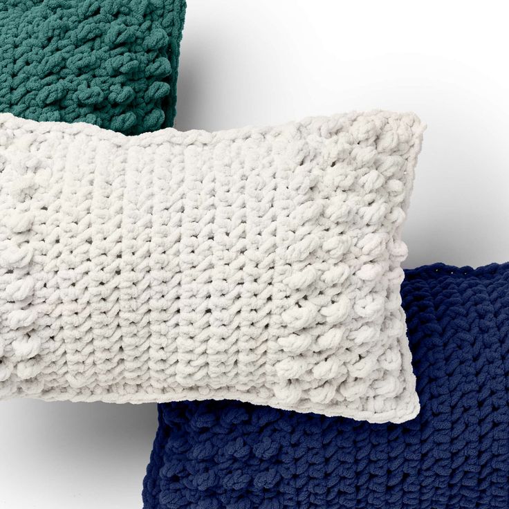 three knitted pillows on top of each other, one blue and the other green