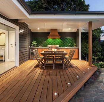 a wooden deck with table and chairs next to an outdoor kitchen on the other side