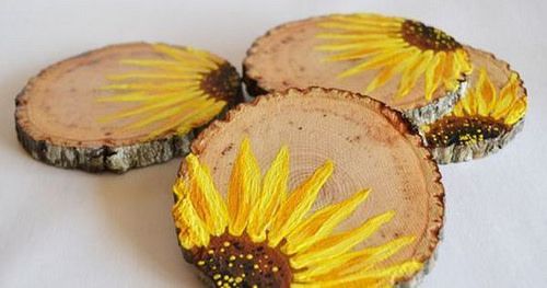 three sunflowers painted on wood slices sitting on a white tablecloth covered surface