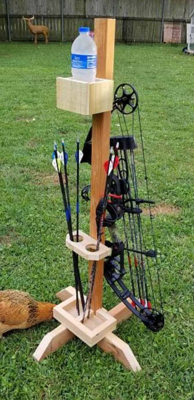 an outdoor archery stand with arrows, bows and water bottle on it in the grass