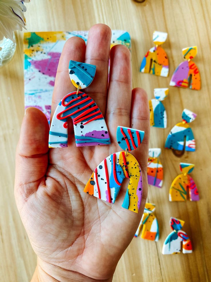 a hand holding several pieces of colorful art on top of a wooden table next to scissors