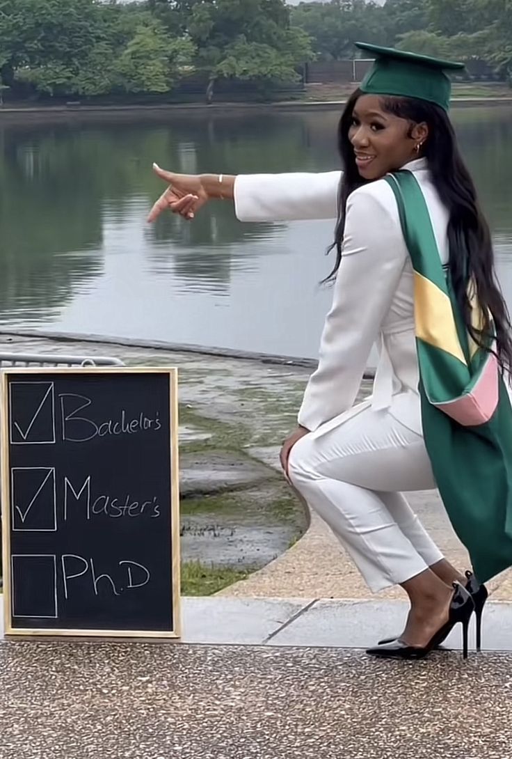 a woman in a graduation gown pointing at a sign