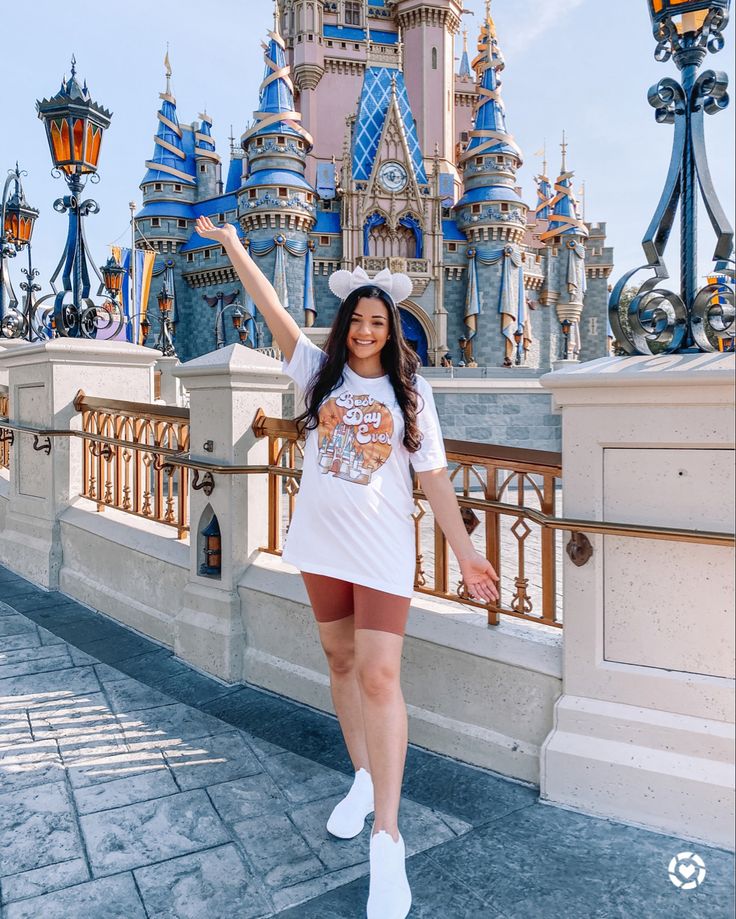 a woman standing in front of a castle with her hand up to the side and arms outstretched