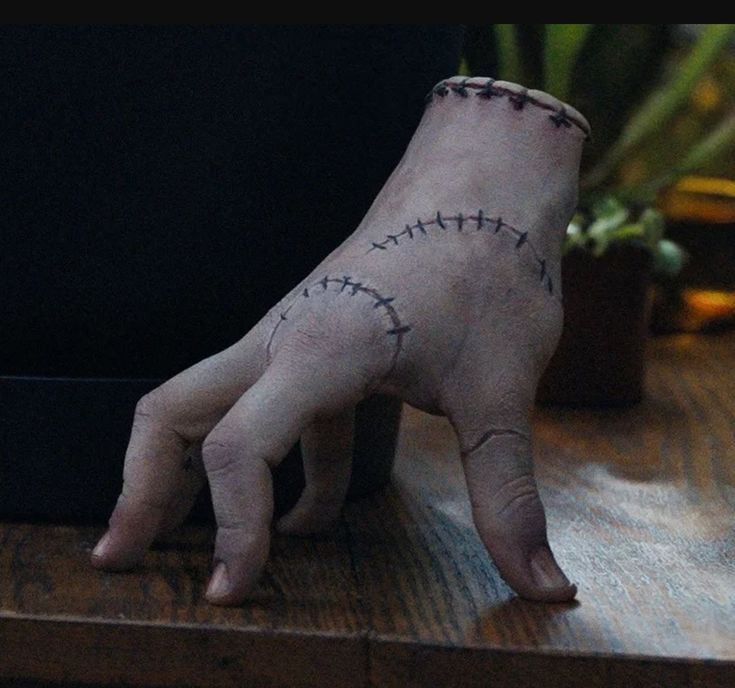 a hand with stitches painted on it sitting on a table next to a potted plant