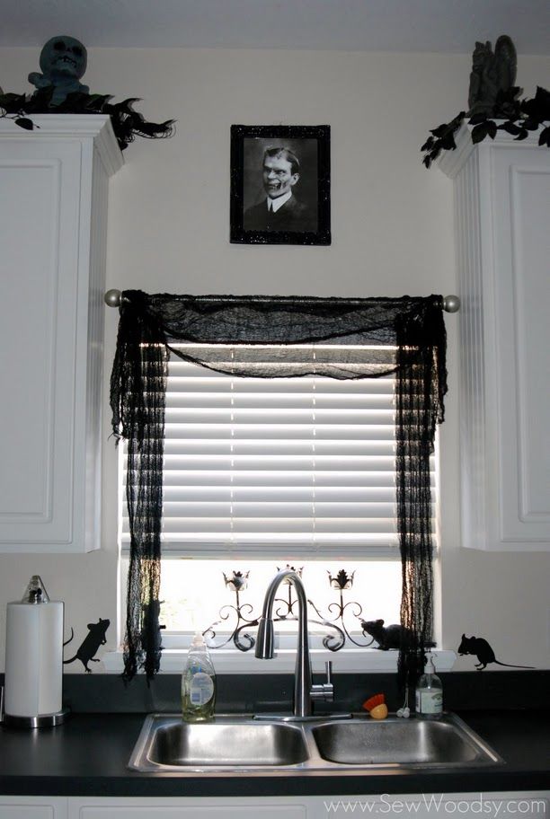 a kitchen sink under a window covered in black and white curtains with the words, decorate with creepy cloth