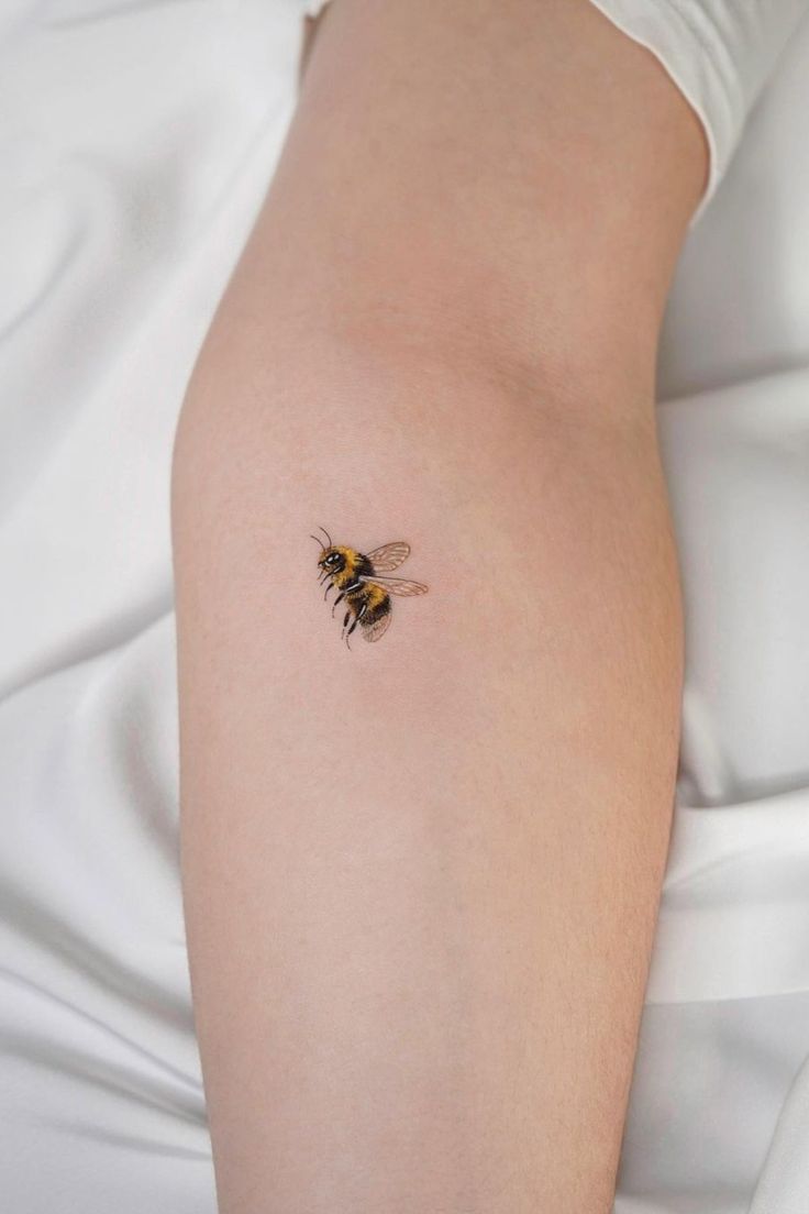 a close up of a person's arm with a bee tattoo on the side