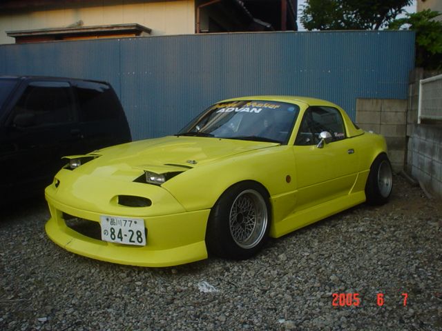 a yellow sports car parked in front of a blue wall and another black car behind it