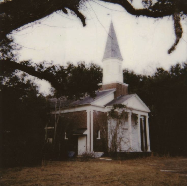 an old white church with a steeple in the middle of it's yard