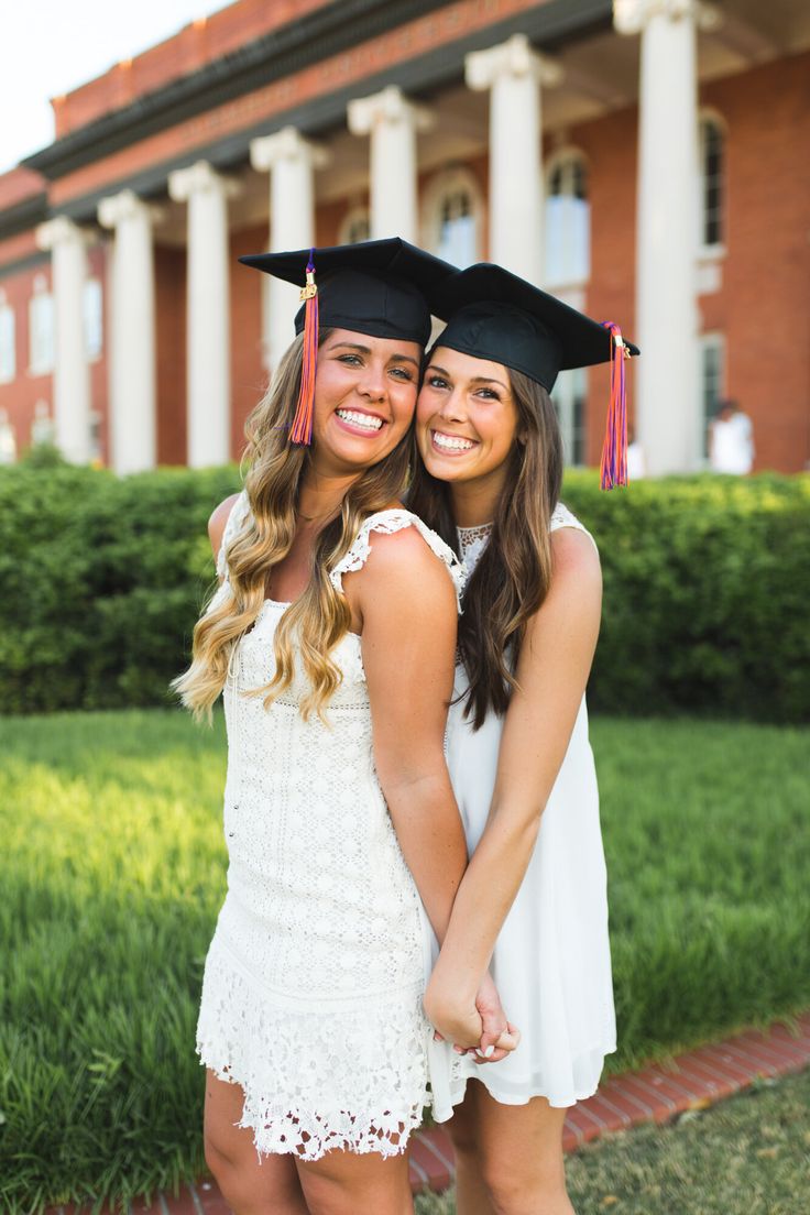 two girls in graduation caps and gowns hugging each other on the grass outside of a building