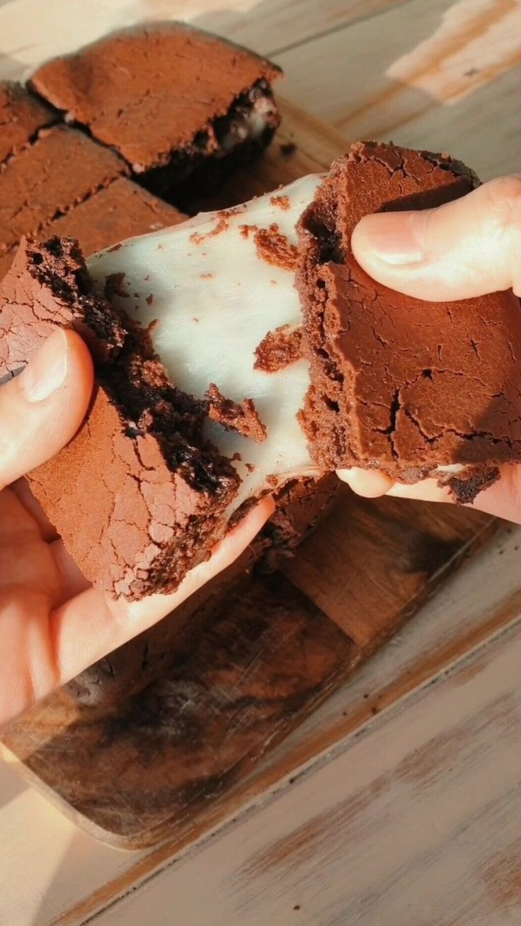 a person holding a piece of brownie with white frosting