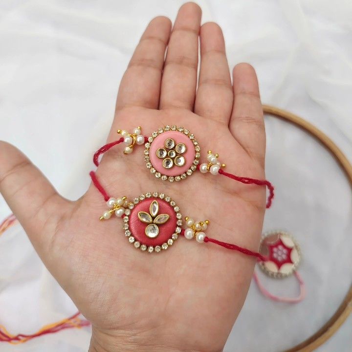 the hand is holding two bracelets that are decorated with red string and gold beads