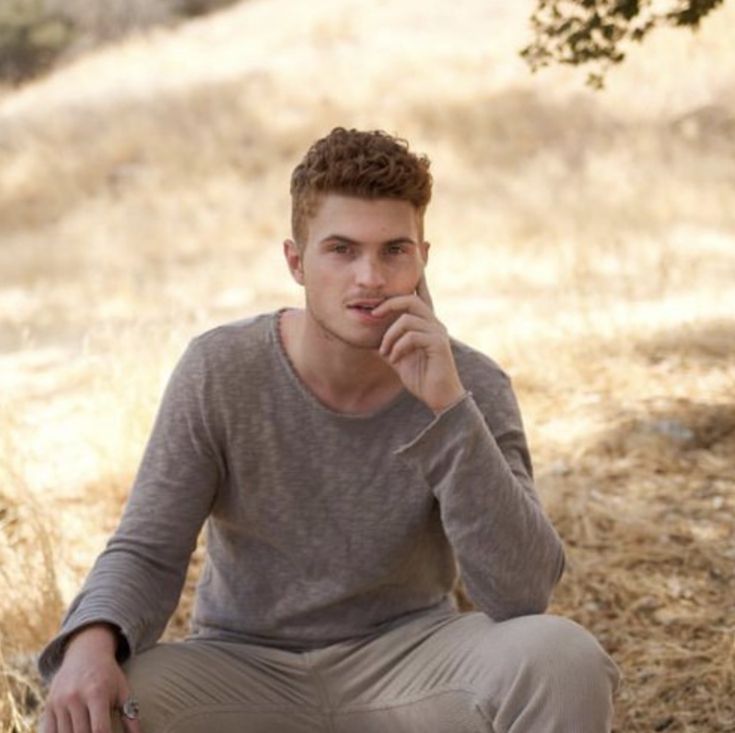 a young man sitting on the ground with his hand to his chin and looking at the camera