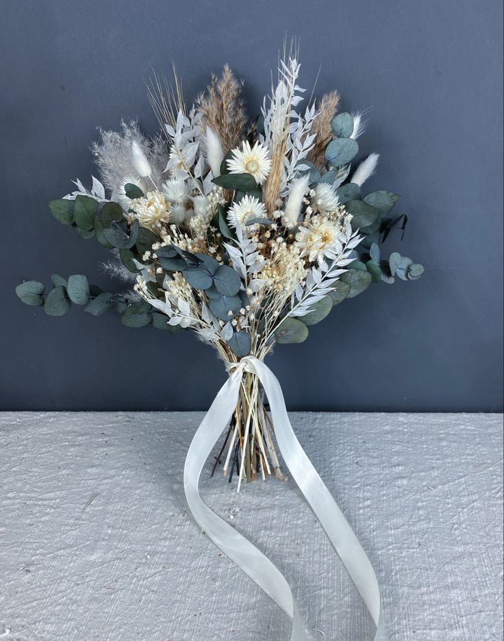 a bouquet of dried flowers in a vase with a ribbon tied around the stems and leaves