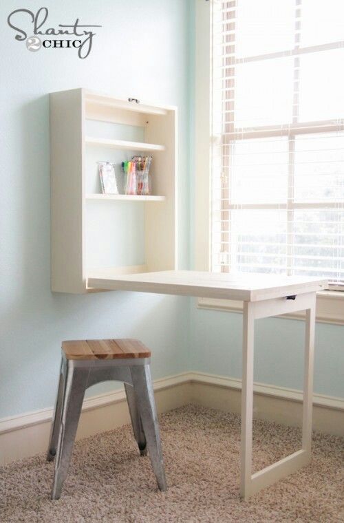 a small white desk with a shelf above it and a stool next to it in front of a window