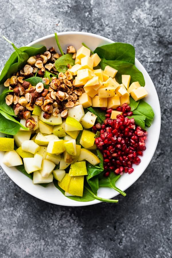 a white bowl filled with spinach, apples, nuts and pomegranate