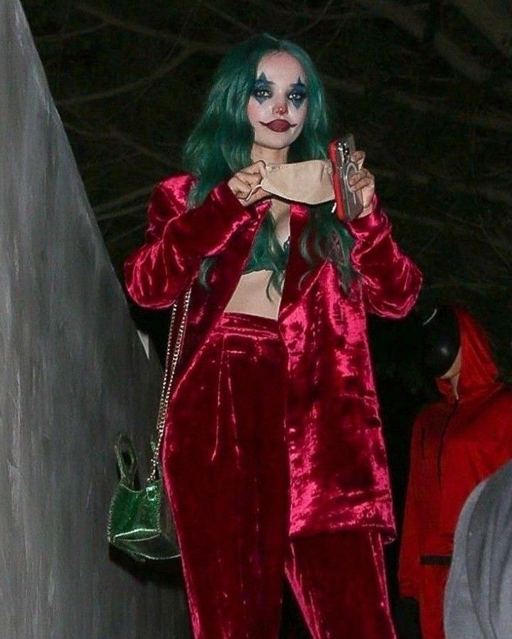 a woman with green hair wearing a red suit and holding a cell phone in her hand