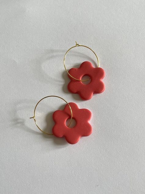 two red flower shaped earrings sitting on top of a white table next to each other