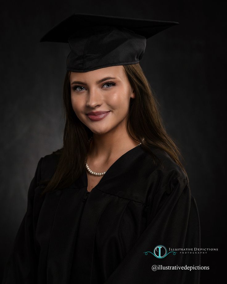 a woman wearing a black graduation gown and smiling at the camera with her hands in her pockets