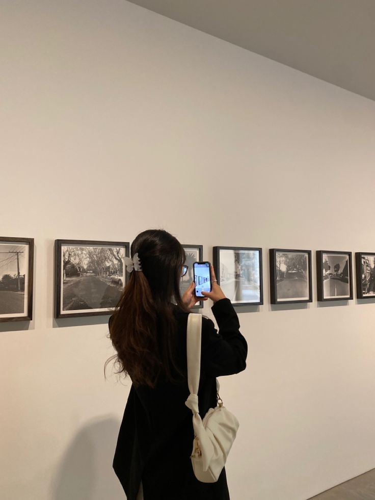 a woman taking a photo of pictures on the wall with her cell phone in hand