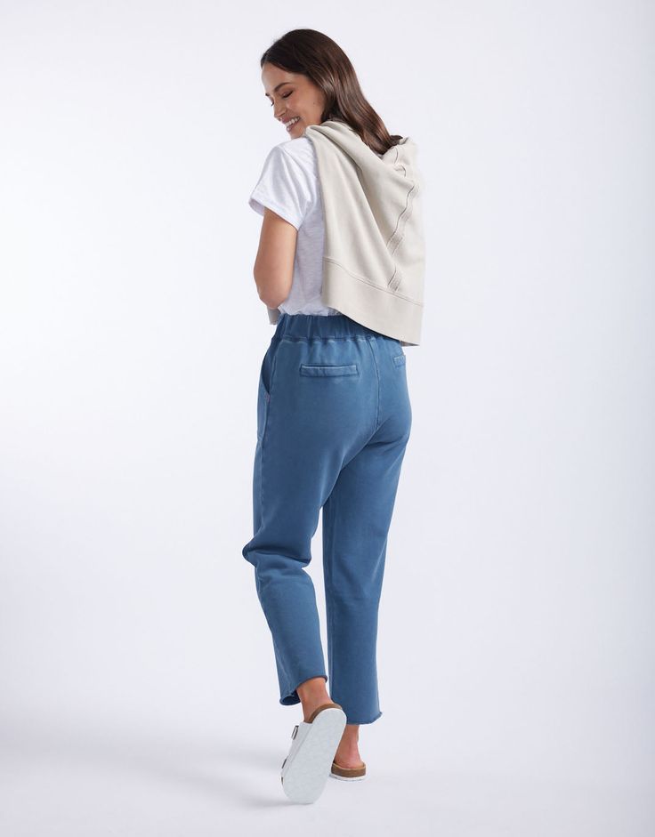 the back view of a woman wearing blue pants and a white t - shirt, with her hands in her pockets