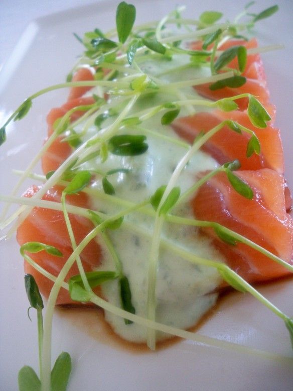 a white plate topped with salmon covered in sauce and green sprout garnish