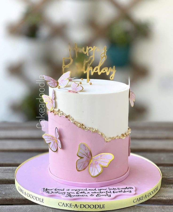 a pink and white cake with gold butterflies on it's side sitting on a wooden table