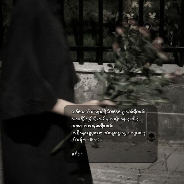 a woman is walking down the street with flowers in her hand and an iron gate behind her