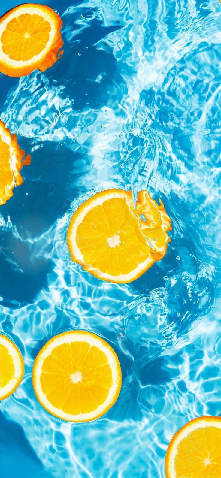 several oranges floating in the water near each other on top of a blue surface