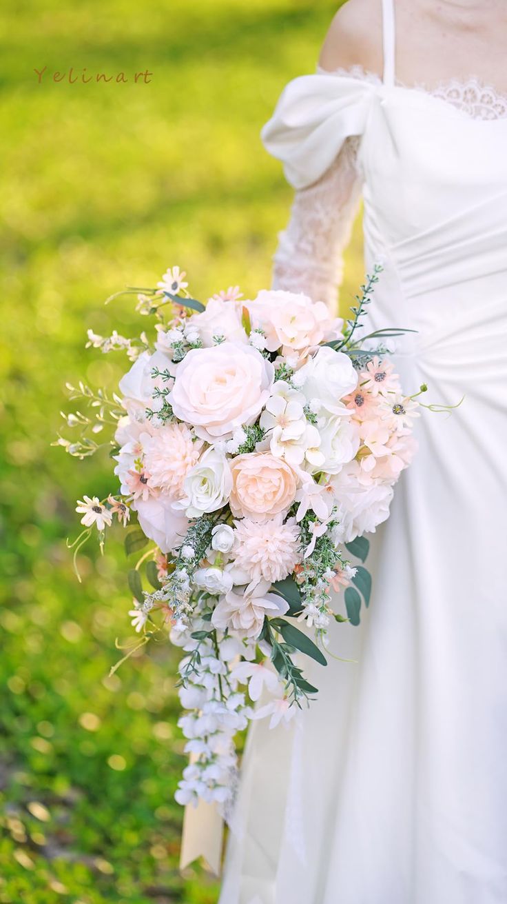 a bride holding a bouquet of white and pink flowers in her hand on the grass