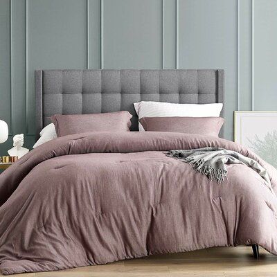 a bedroom with grey walls and a bed covered in purple comforter covers, pillows and blankets